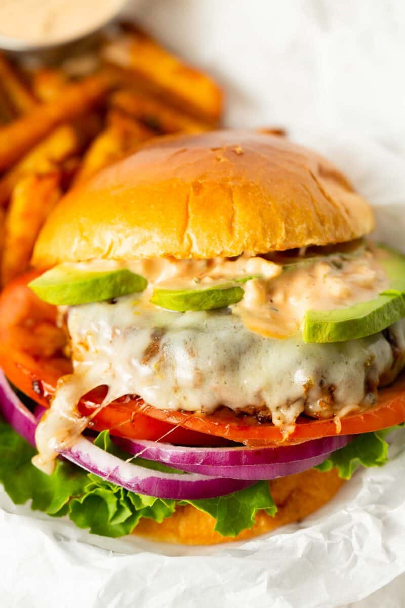 up close image of california burger with melted cheese on top of the burger patty sandwiched between brioche buns, loaded with fresh avocado slices, burger sauce, tomato, onion, and lettuce.