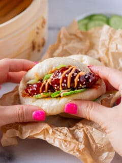 chicken bao bun being held by hands with bright pink nail polish