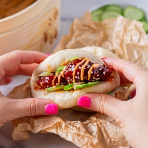 chicken bao bun being held by hands with bright pink nail polish