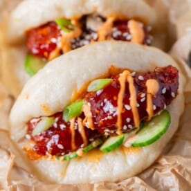 chicken bao bun garnished with an orange sauce, sesame seeds, and fresh cucumbers