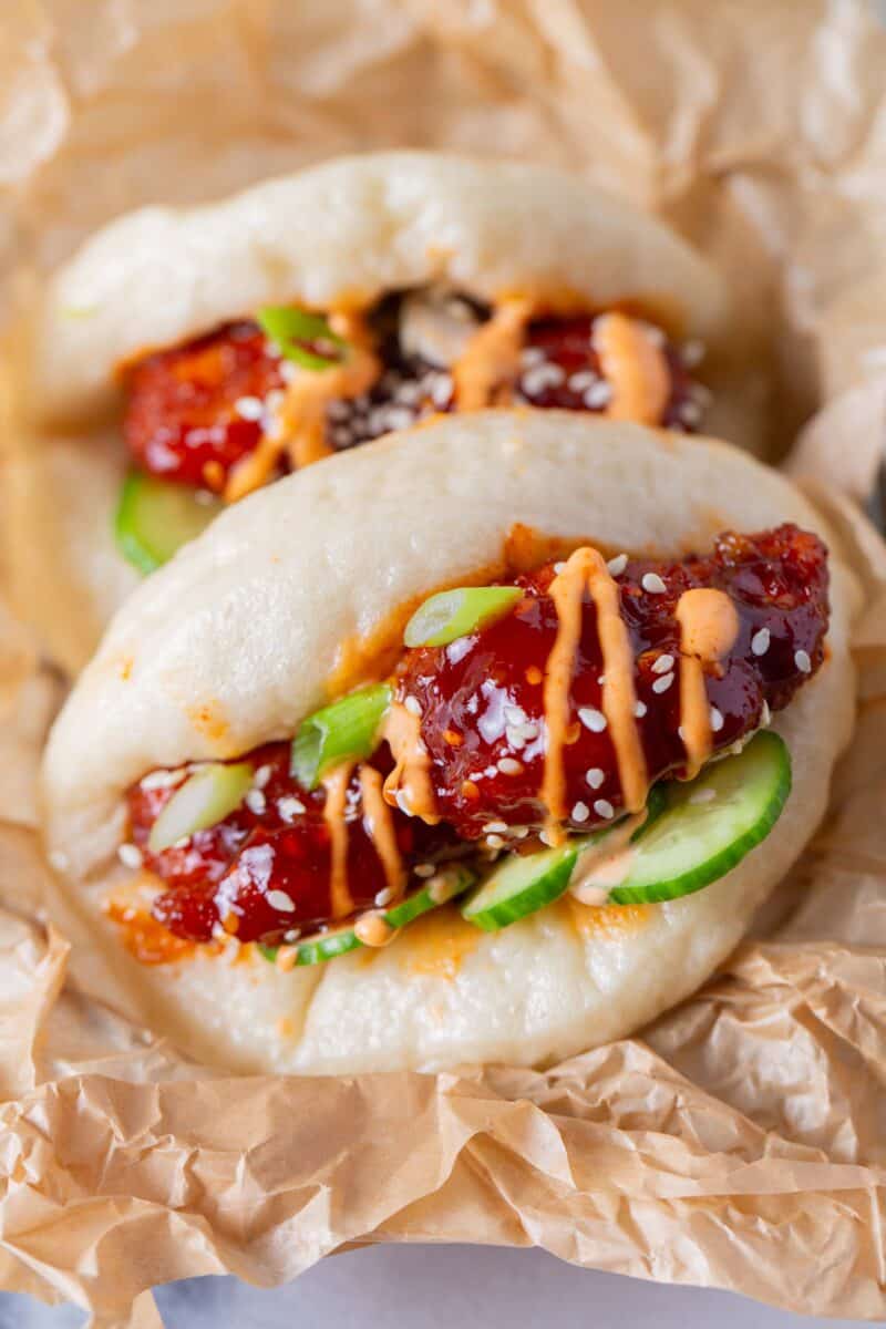 chicken bao bun garnished with an orange sauce, sesame seeds, and fresh cucumbers