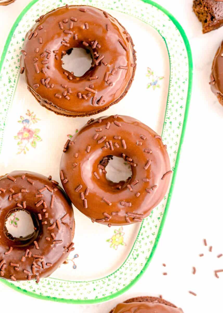 three chocolate frosted donuts are placed on a white platter