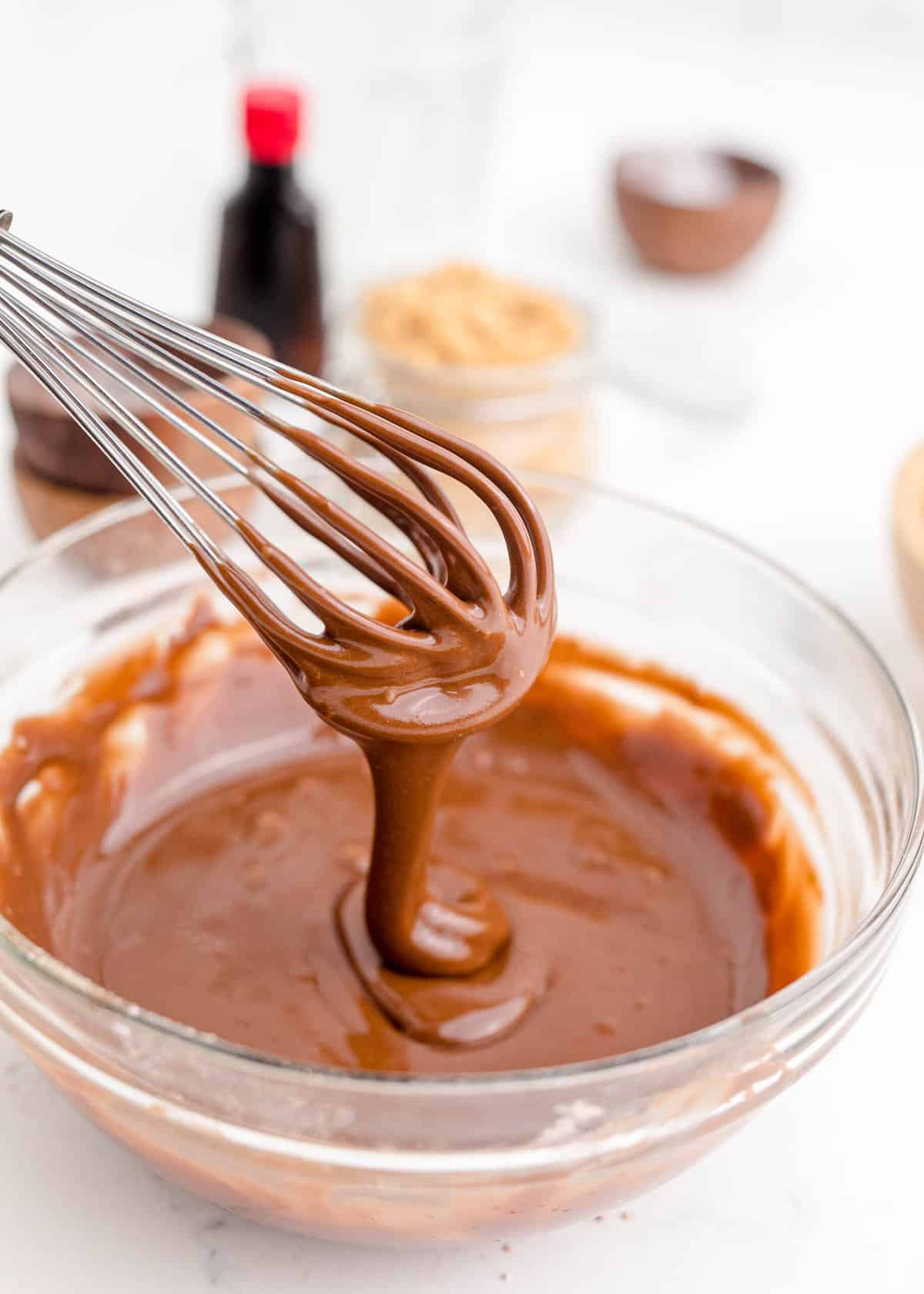 a whisk is drizzling frosting over a full mixing bowl of more frosting