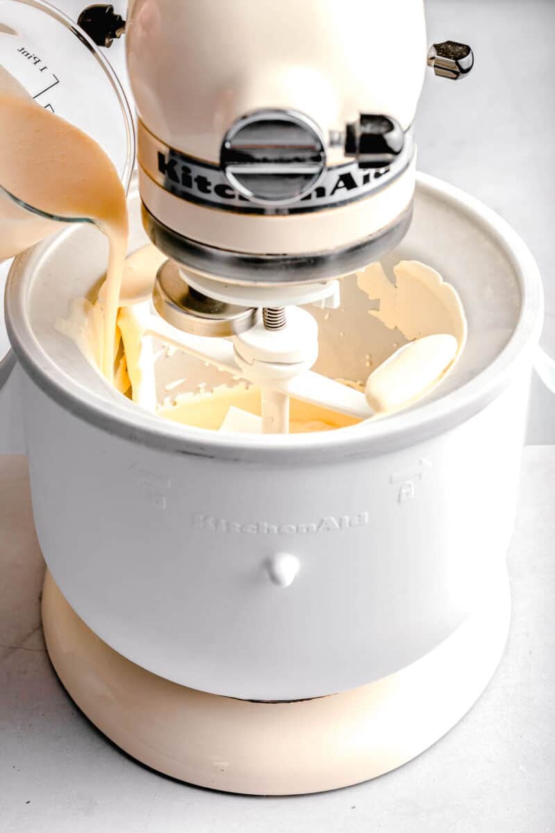 ice cream mixture being poured into ice cream maker attachment on a white kitchenaid stand mixer