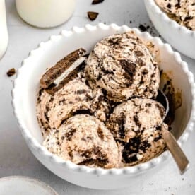 a white bowl of cookies and cream ice cream with 4 scoops and a metal spoon