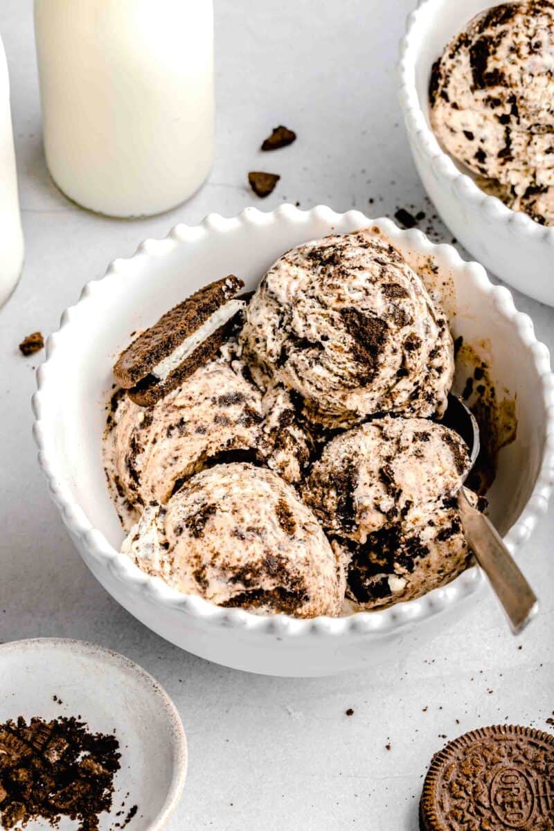 a white bowl of cookies and cream ice cream with 4 scoops and a metal spoon