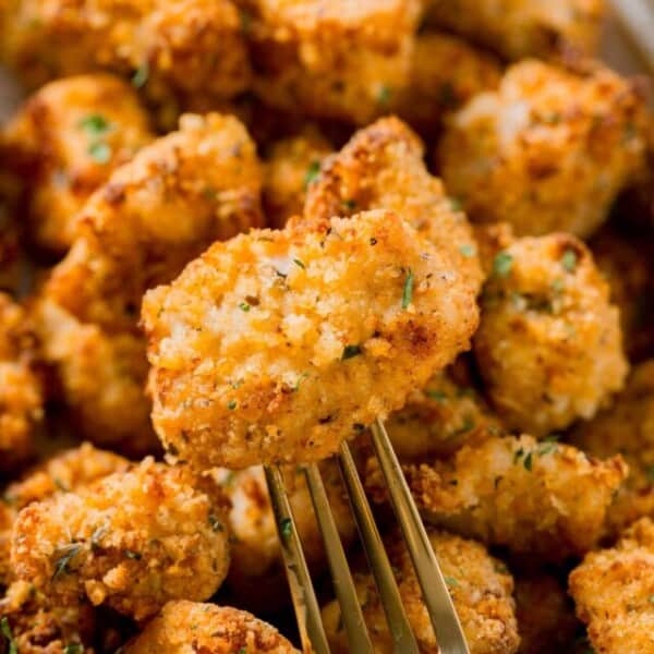 an air fried chicken nugget on a gold fork laying on top of other chicken nuggets