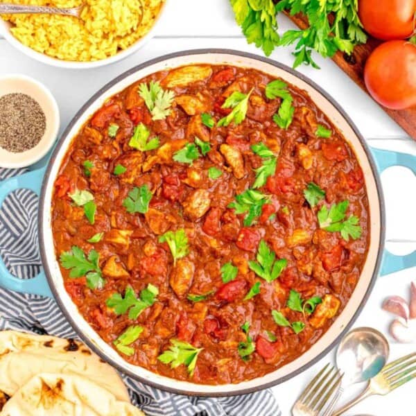 madras curry in a cast iron pot garnished with fresh parsley next to a linen towel with naan