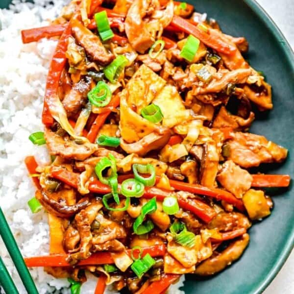 Mu shoo chicken on a plate with white rice and chopsticks.