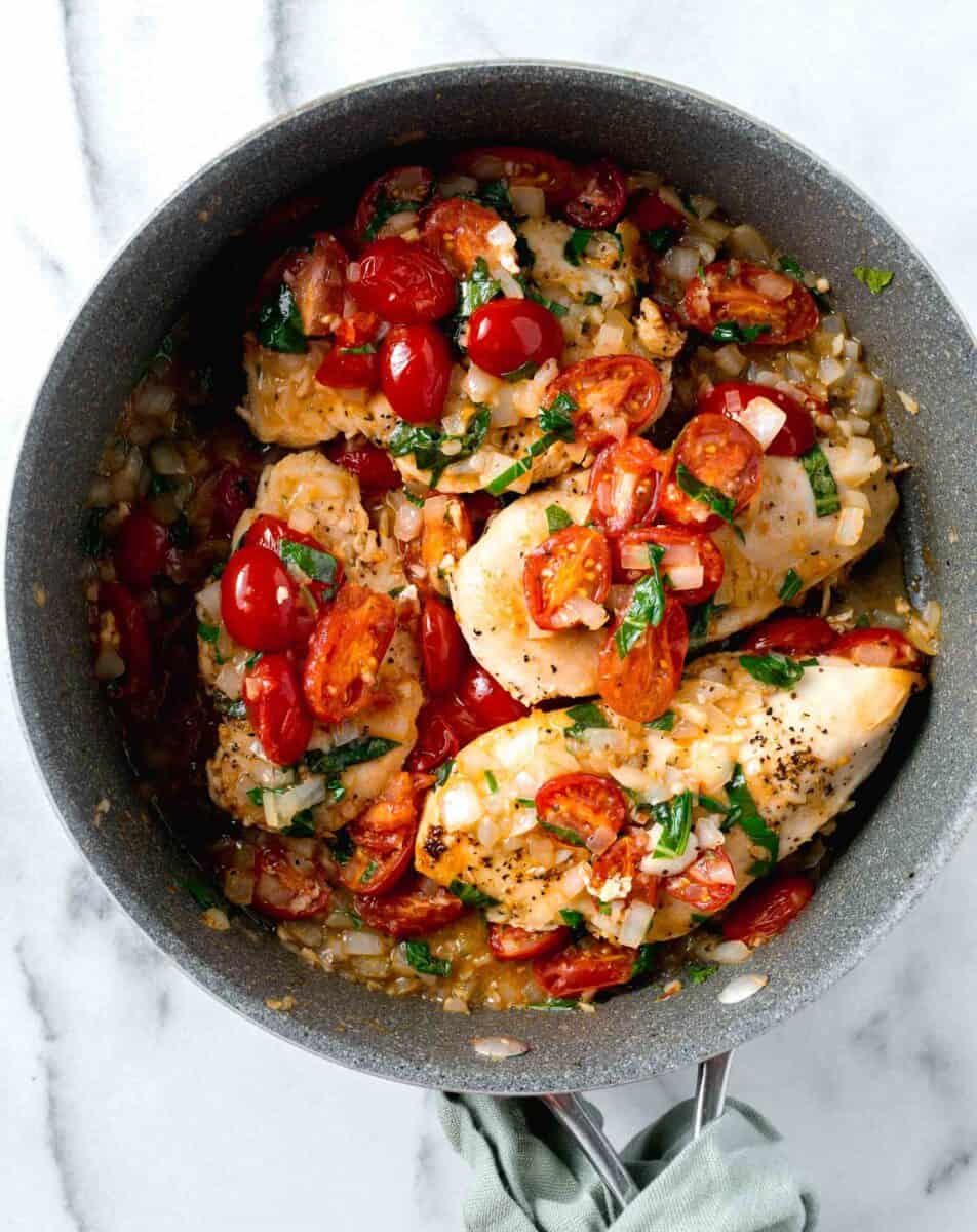one pan garlic tomato basil chicken in skillet with fresh tomatoes, basil, and onions on top of the chicken breasts