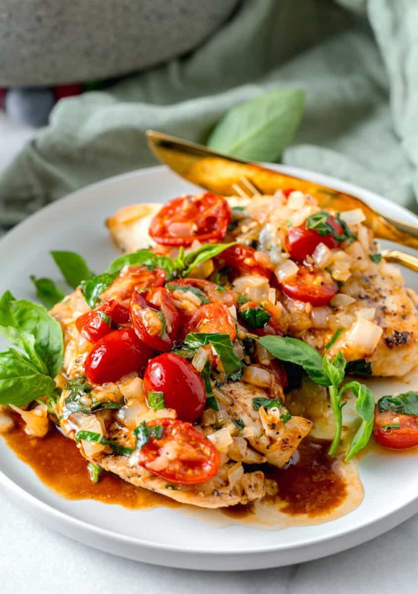 chicken breasts plated on a white plate with fresh tomatoes, basil, onions on top with balsamic vinegar drizzled.