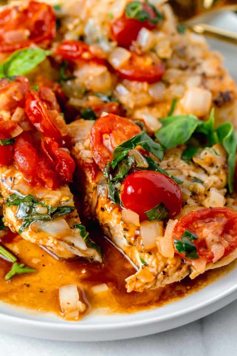 chicken breast sliced in half with grape tomatoes and basil and onions on top with balsamic vinegar around the sliced chicken