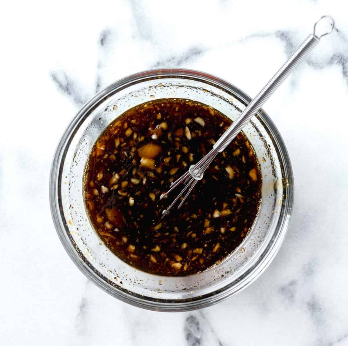 sauce for honey garlic lemon pepper chicken thighs in a clear bowl whisked together with a metal whisk