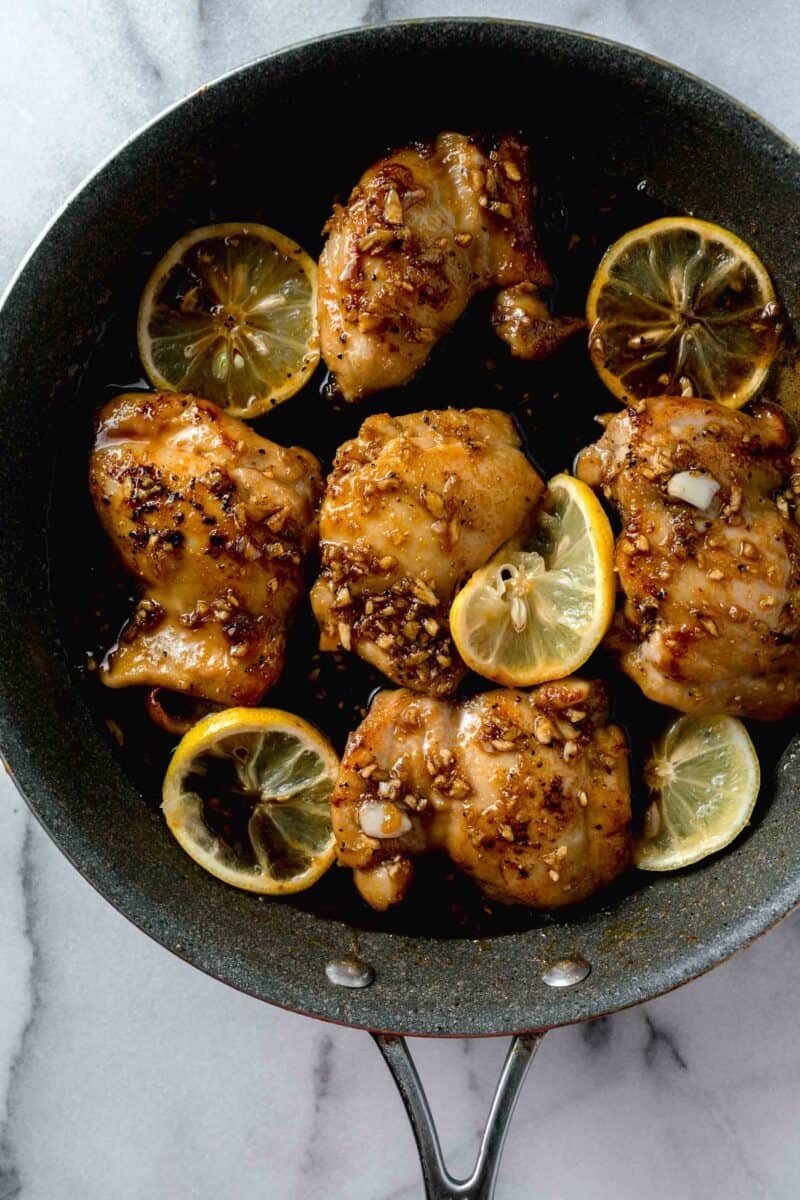 honey garlic sauce poured on top of seared chicken thighs and lemon slices in a grey skillet