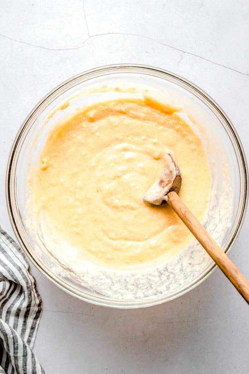 batter for lemon blueberry cupcakes mixed together with a wooden spoon in a clear bowl