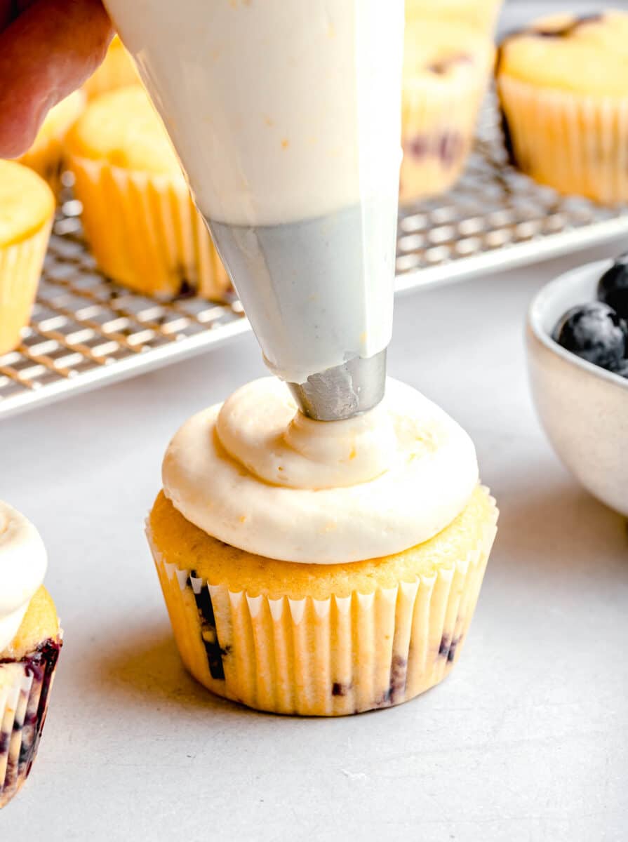piping lemon cream cheese frosting on a lemon blueberry cupcake