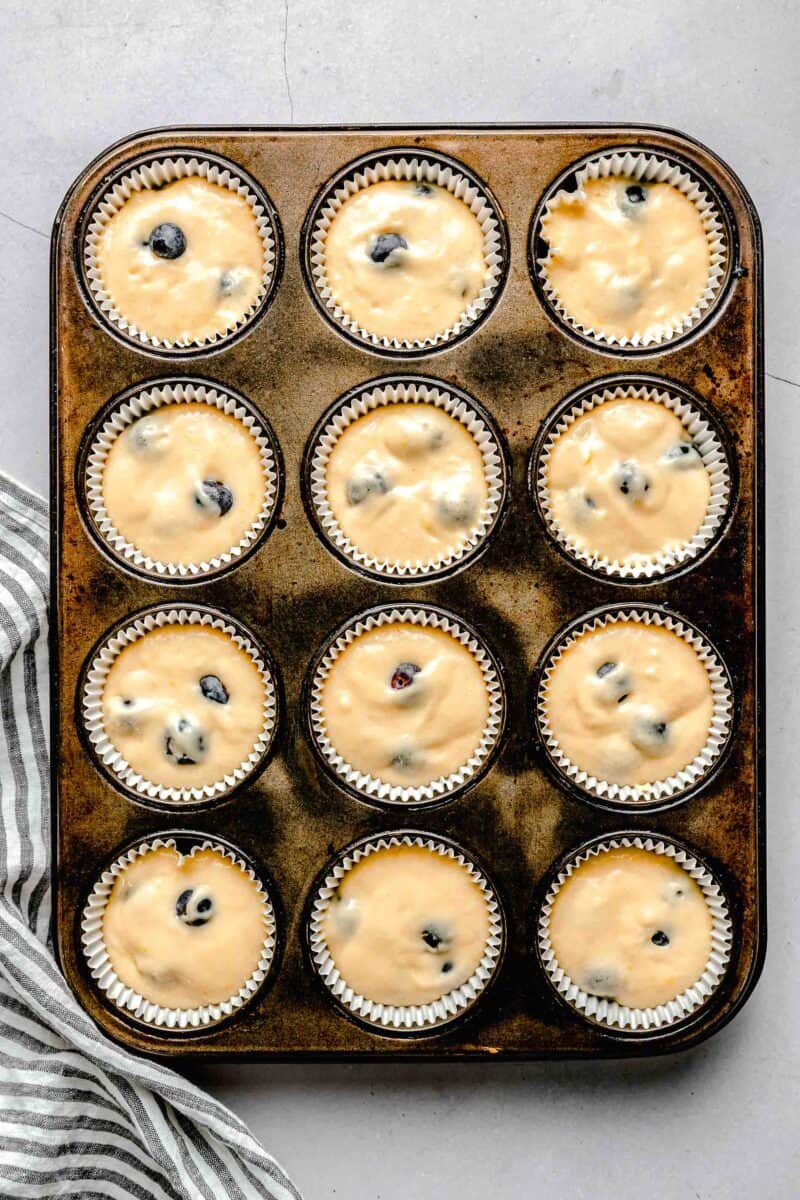 muffin liners filled with lemon blueberry cupcake batter in an aged muffin tin