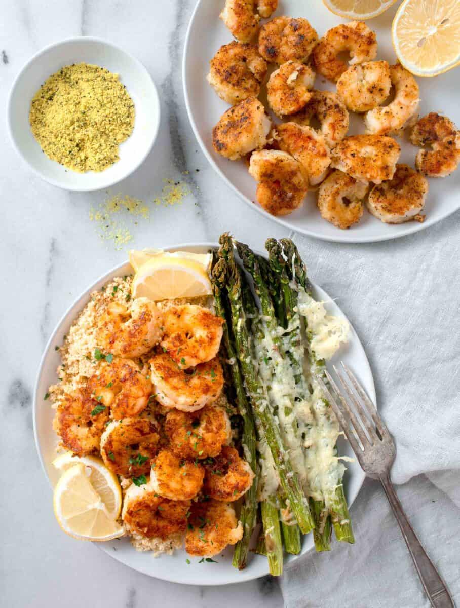 lemon pepper shrimp on a white plate on top of couscous with parmesan asparagus and lemon slices