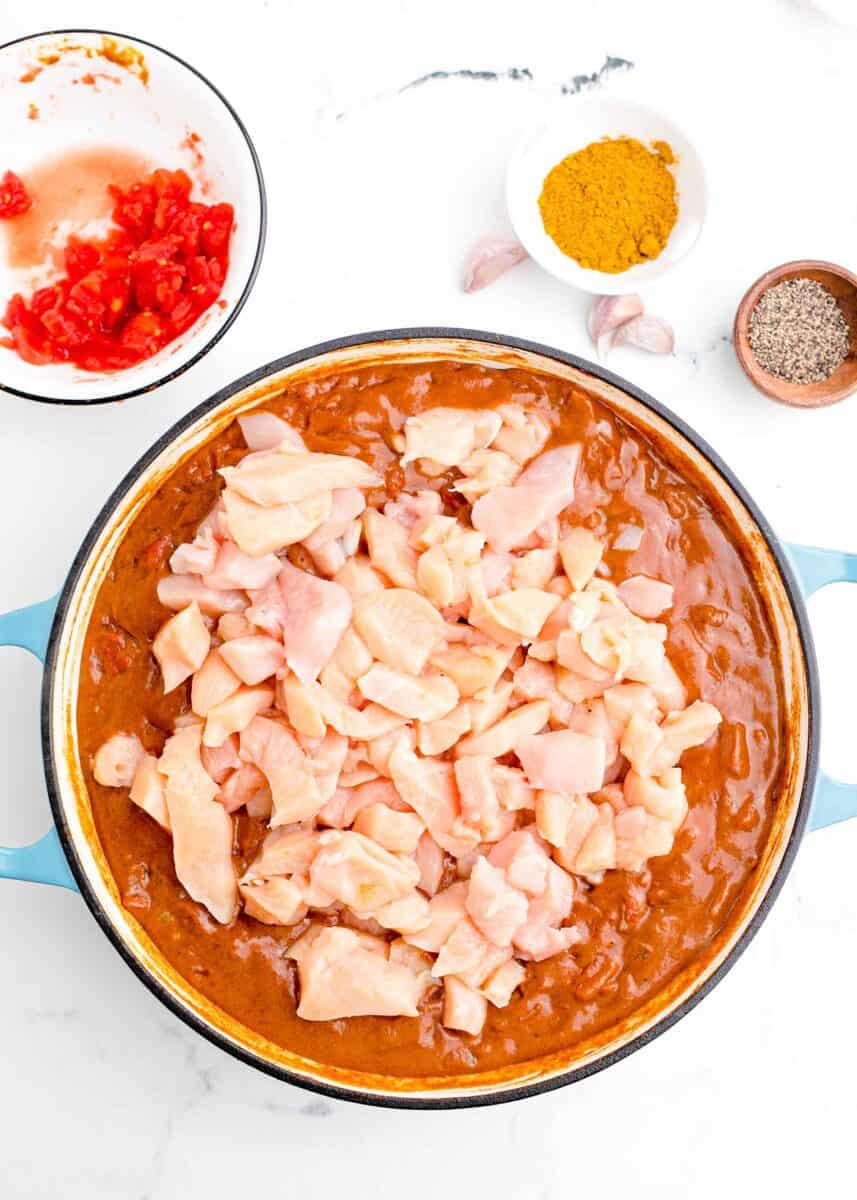 raw chicken pieces added to a tomato-base curry in a cast iron pot
