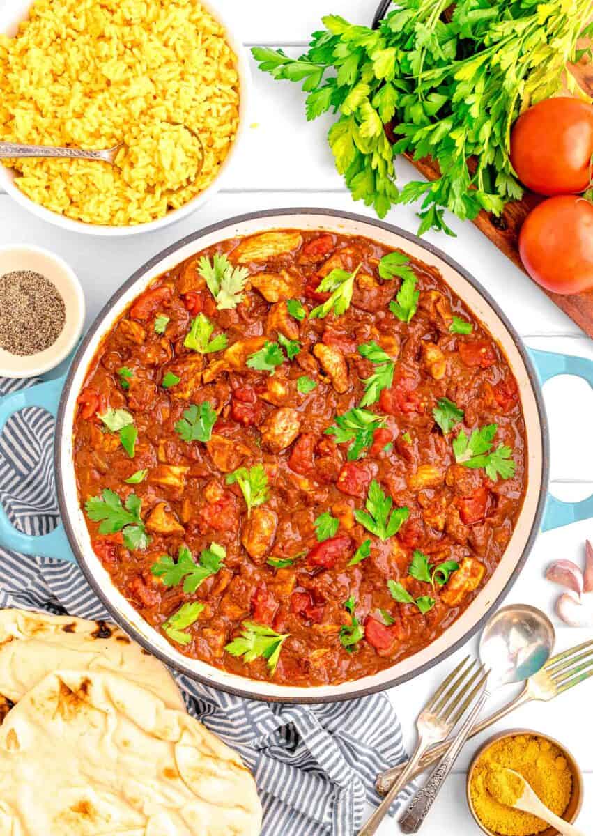 madras curry in a cast iron pot garnished with fresh parsley next to a linen towel with naan