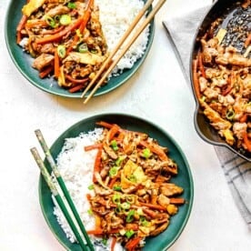 Mu shoo chicken served on plates with white rice and chopsticks.