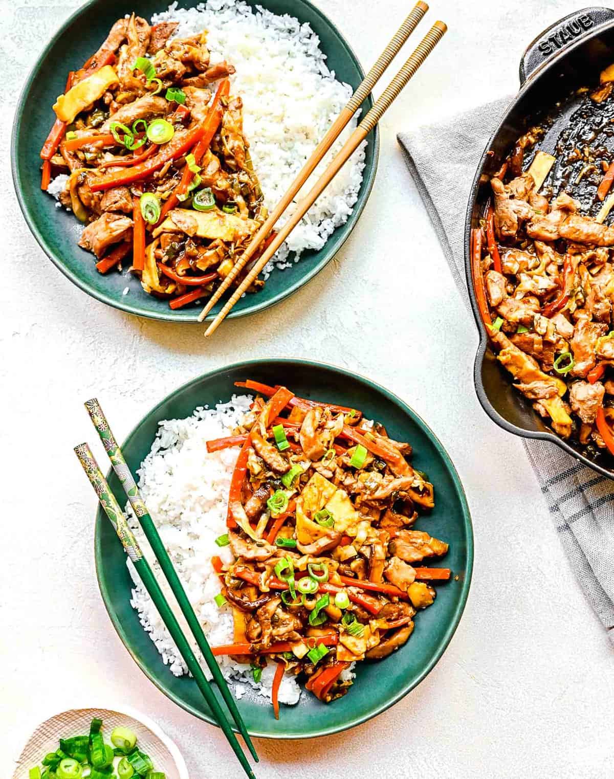 Mu shoo chicken served on plates with white rice and chopsticks.