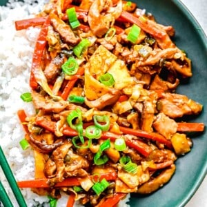 Mu shoo chicken on a plate with white rice and chopsticks.