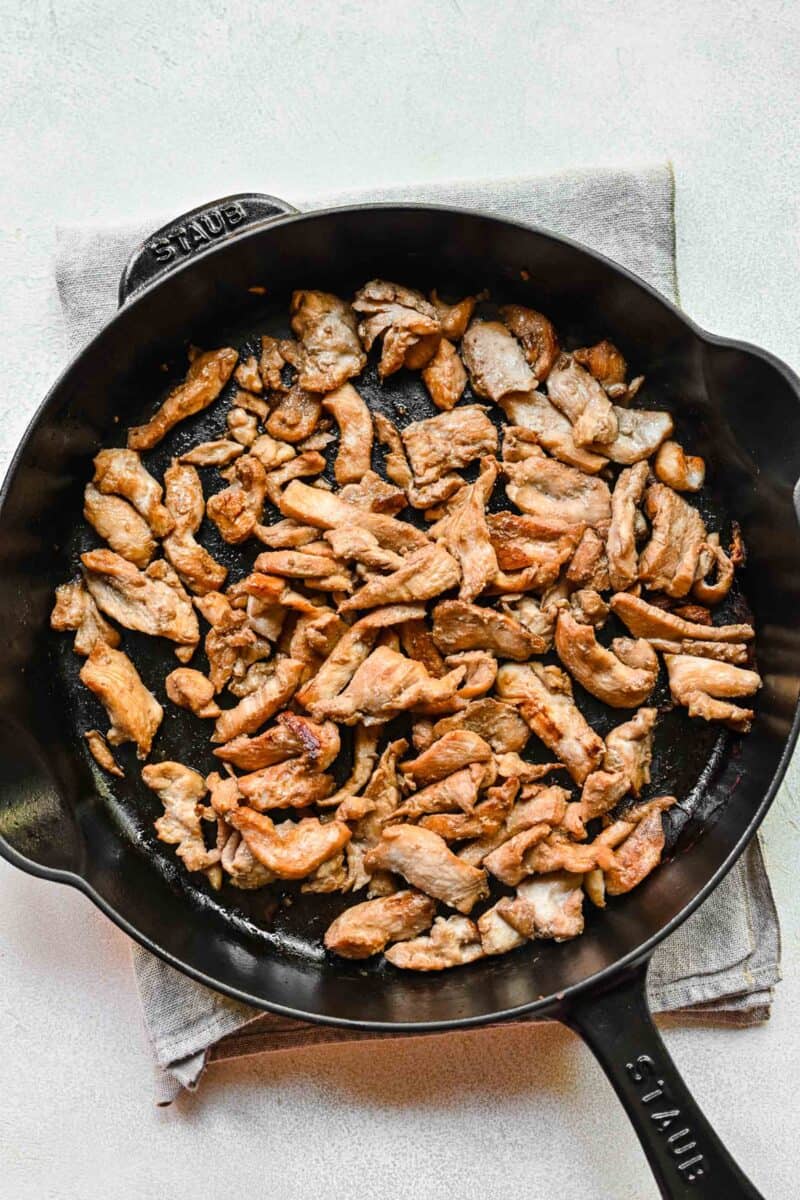 Browning thin slices of chicken in a pan.