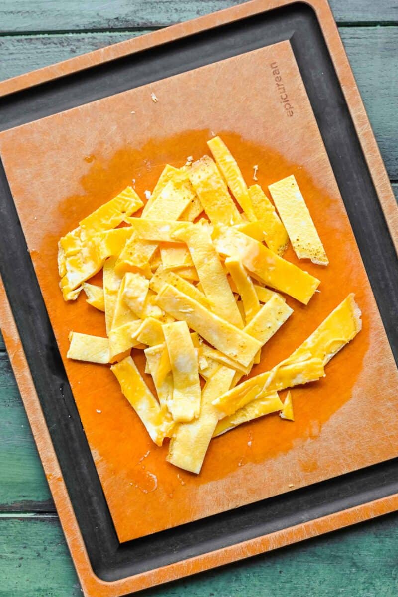 Sliced strips of cooked egg on a cutting board.