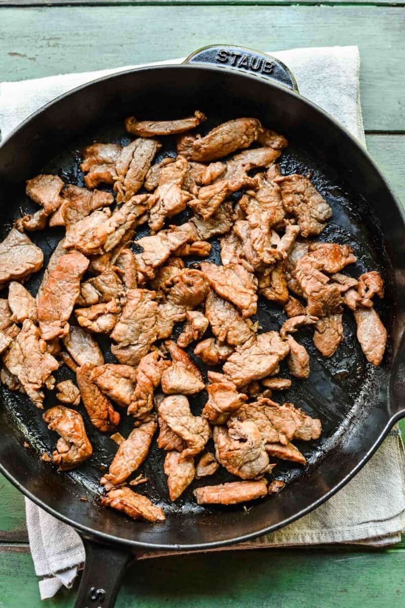 Browning thinly sliced pork in a pan.
