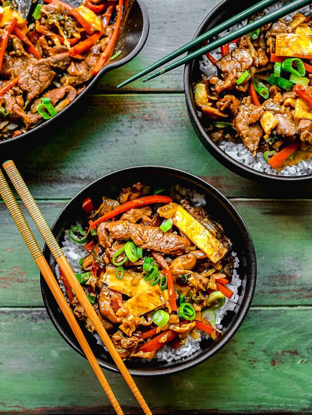 Overhead of 2 bowls of moo shu pork with chopsticks near a pan full of mu shu pork.