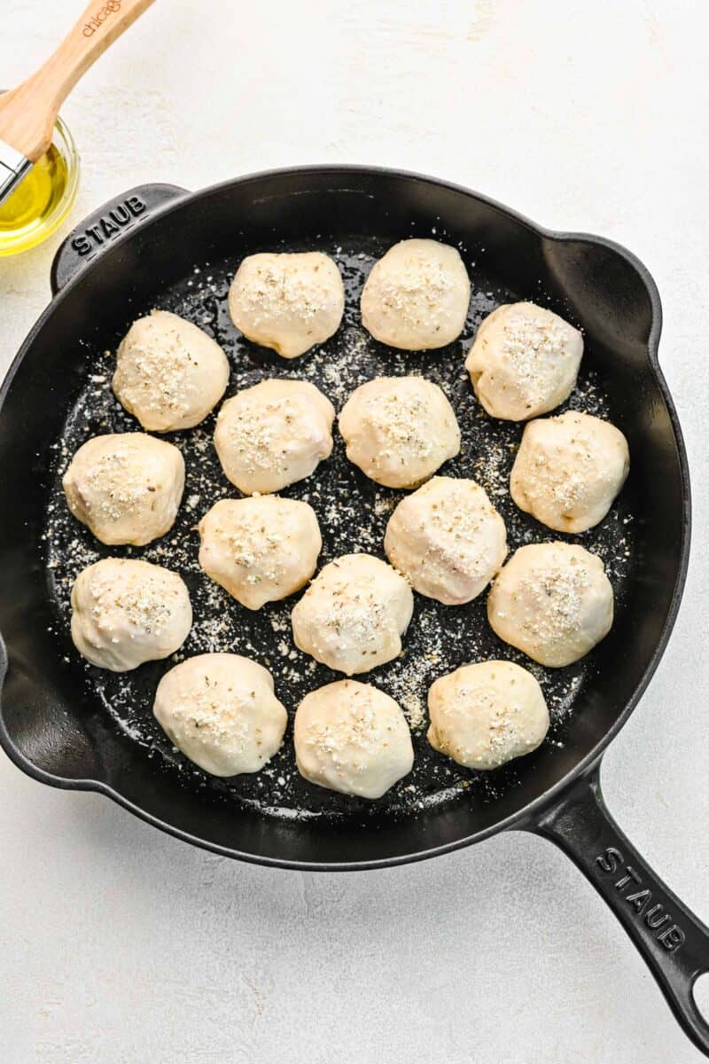 Pizza bites brushed with olive oil and sprinkled with parmesan seasoning in a skillet ready to be baked.