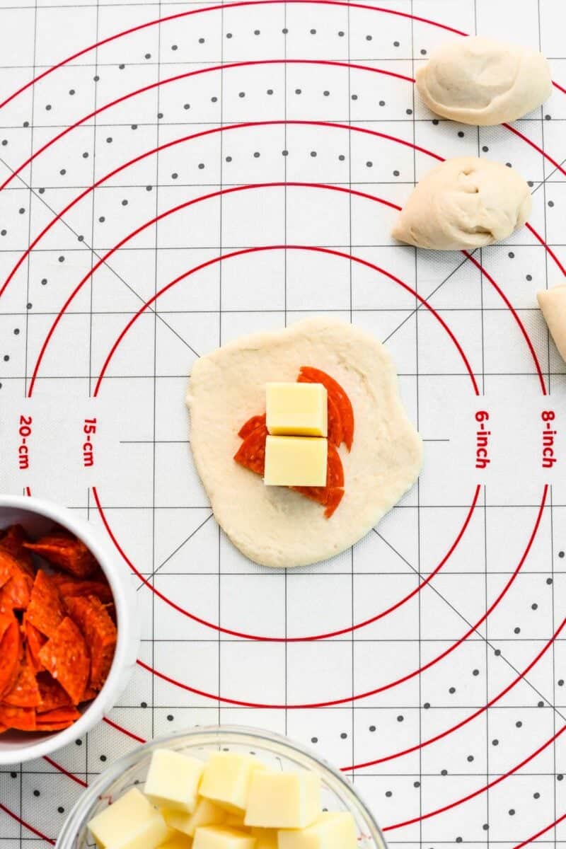 Positioning mozzarella and pepperoni in the center of a circle of pizza dough.