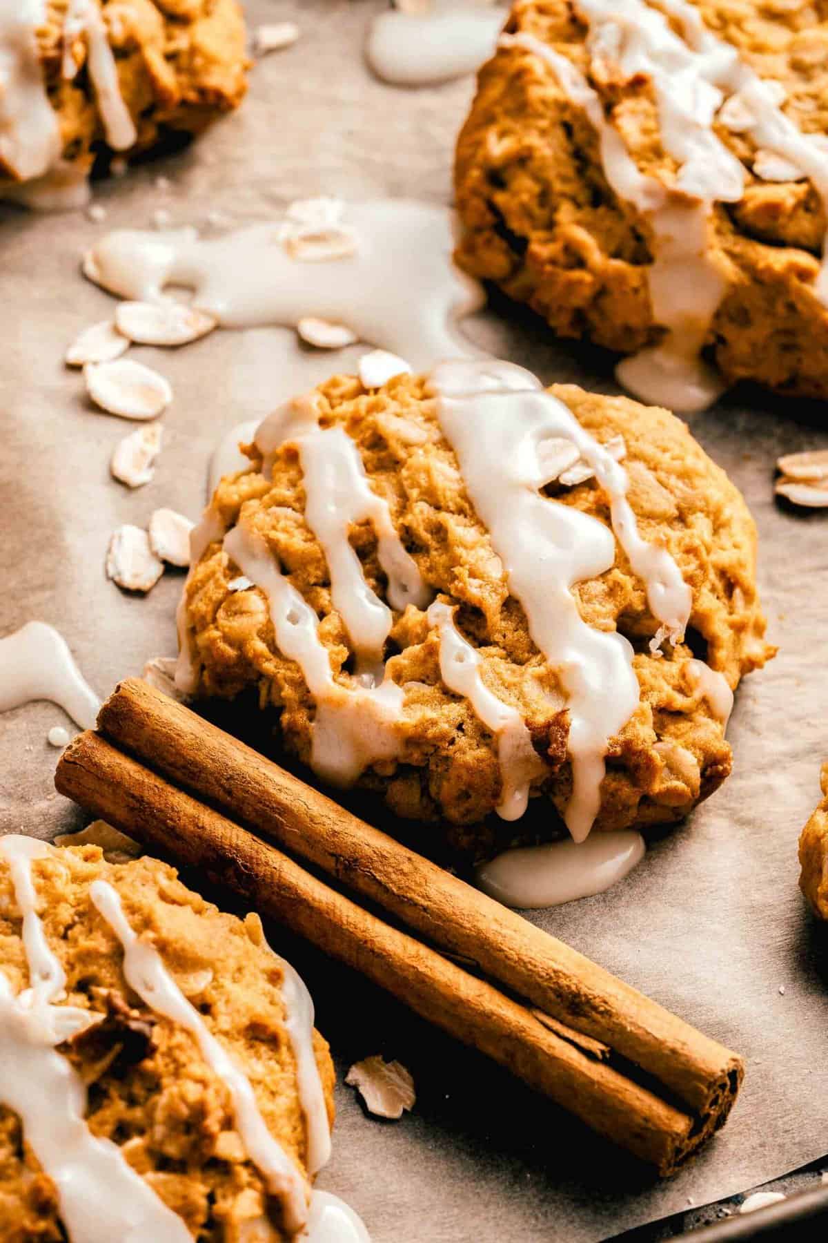 Glazed pumpkin oatmeal cookies on a sheet of parchment paper next to a cinnamon stick.