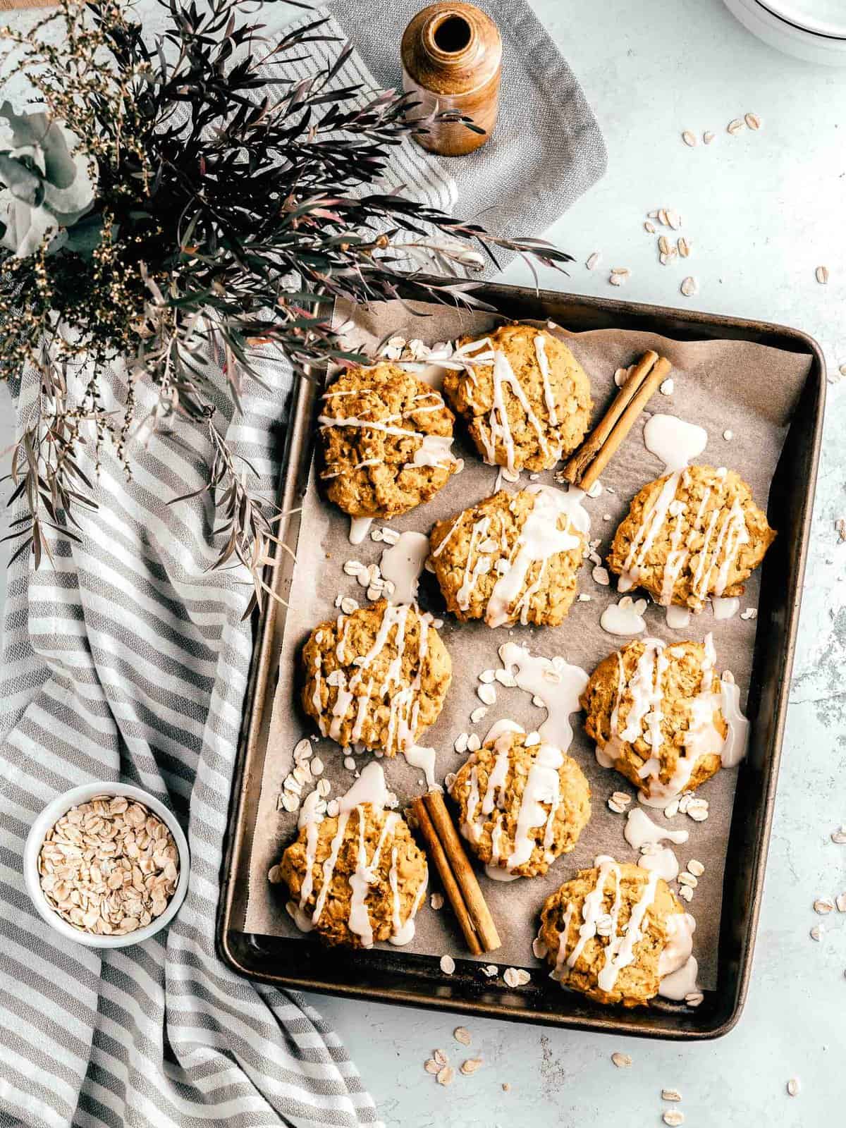 Overhead view of iced pumpkin oatmeal cookies on a baking sheet placed on top of a tea towel.