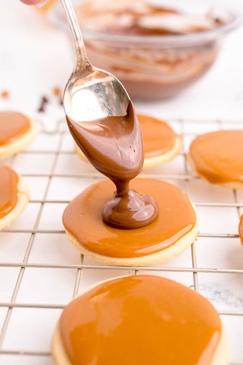 chocolate is being drizzled onto a caramel covered cookie