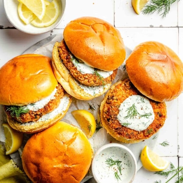 several salmon burgers are placed next to lemon dill mayo and lemon wedges