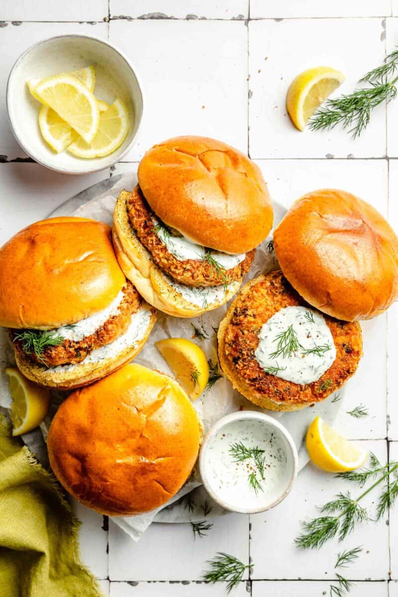 several salmon burgers are placed next to lemon dill mayo and lemon wedges