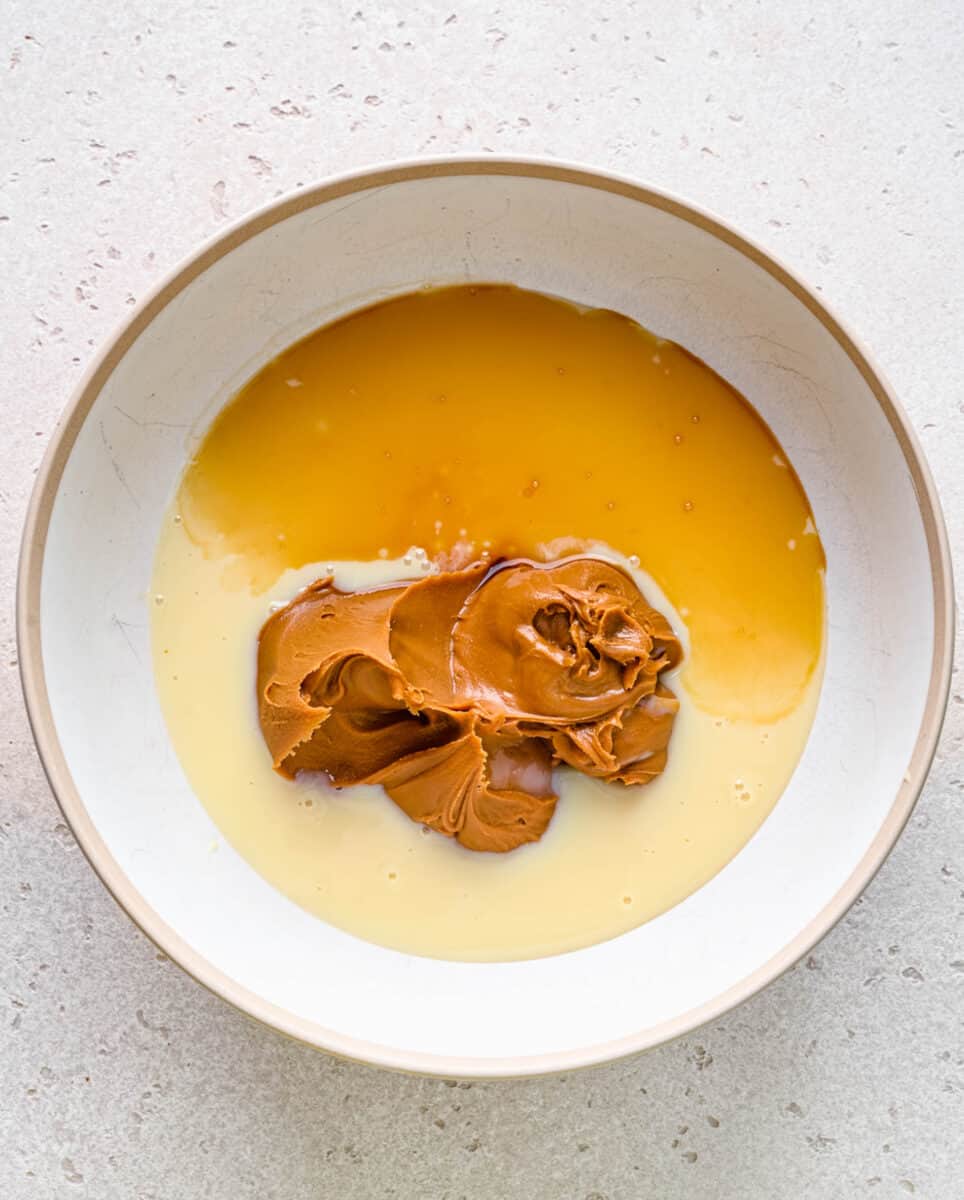 Adding condensed milk, cookie spread, and vanilla extract to a bowl.