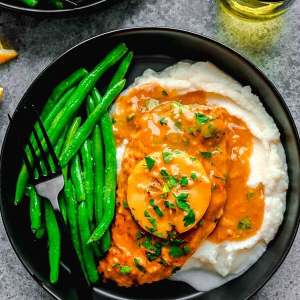 Chicken francese served on a plate over mashed potatoes with green beans.