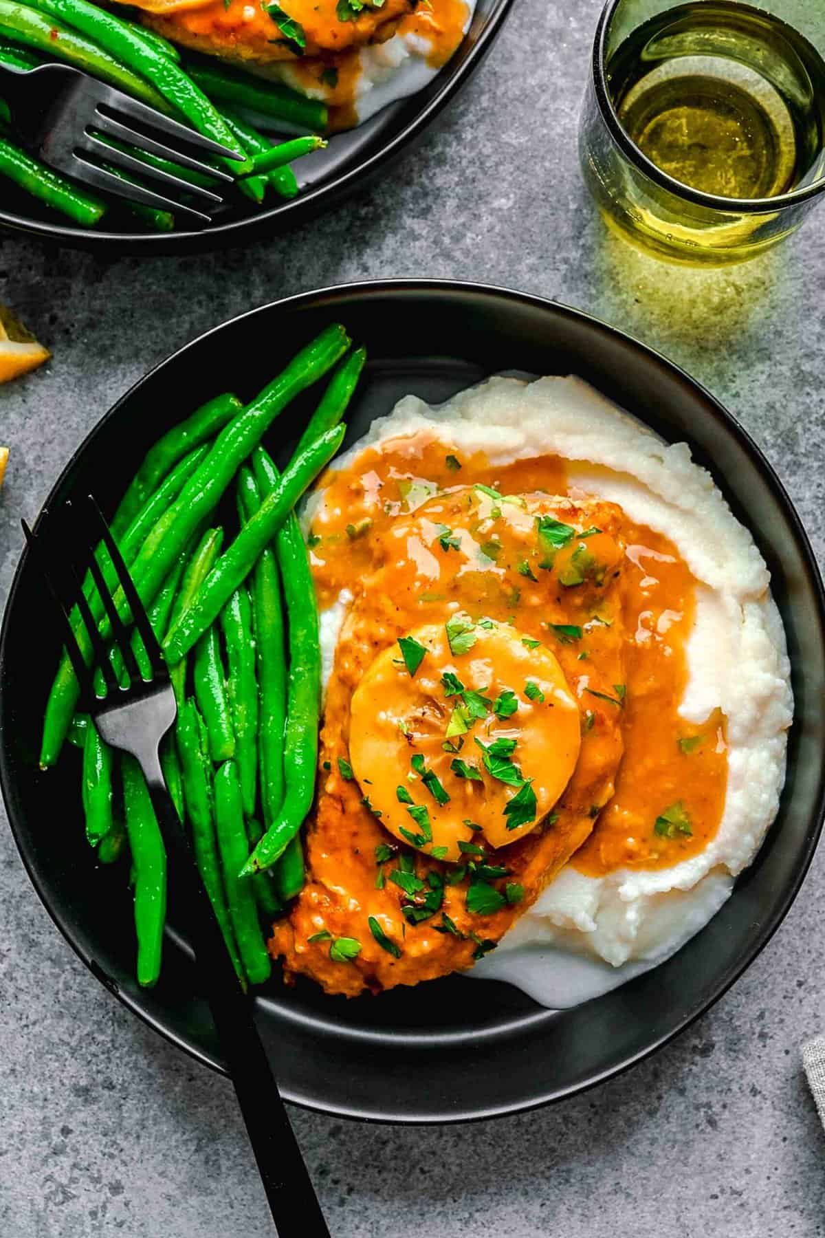 Chicken francese served on a plate over mashed potatoes with green beans.