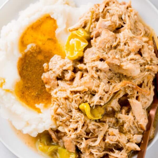 mississippi chicken on a white rimmed plate and mashed potatoes and gravy with a copper metal fork
