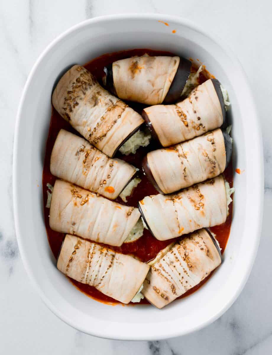 rolled eggplant slices are placed in a white casserole dish