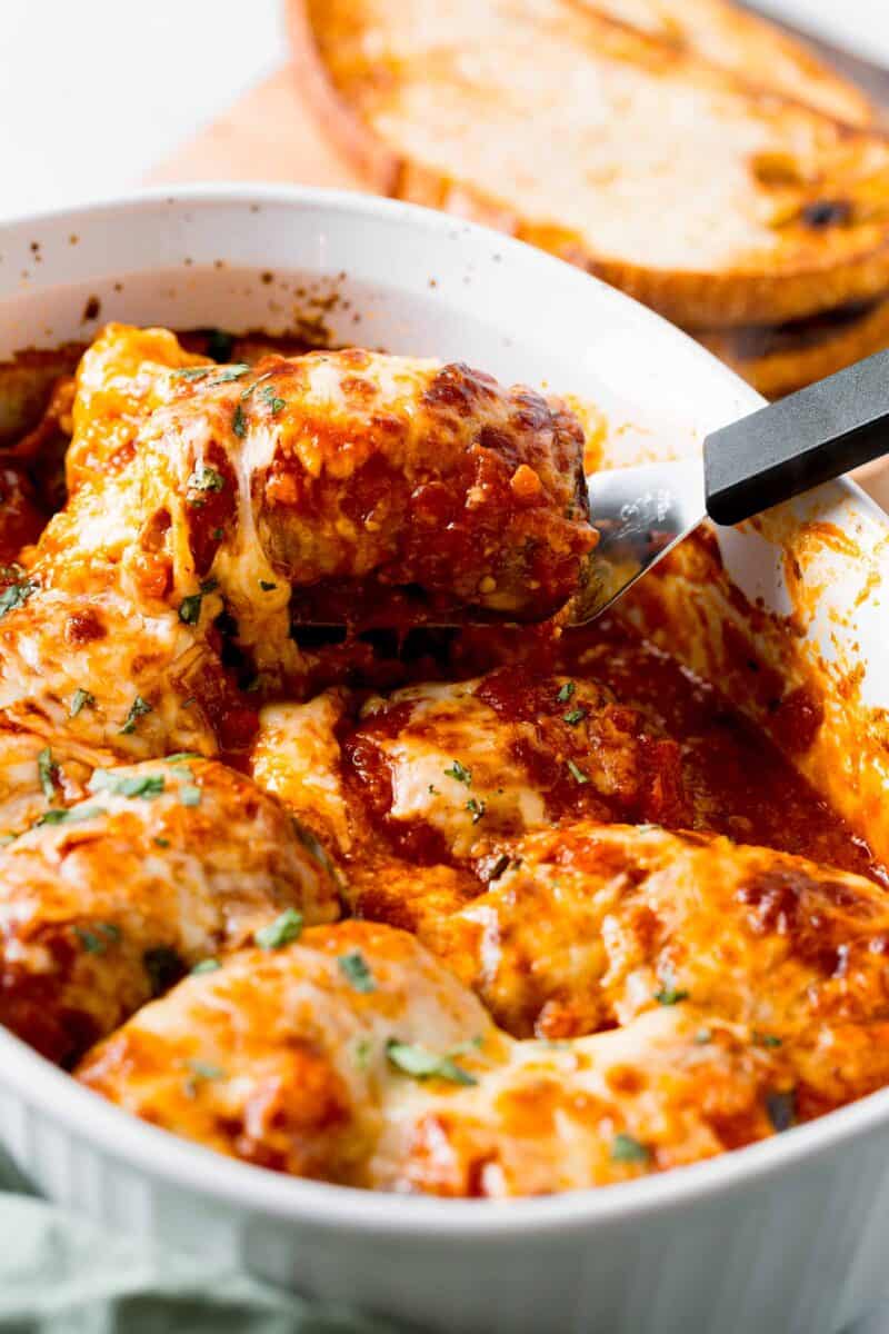 a serving of eggplant rollatini is being lifted from a baking dish