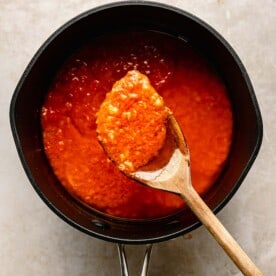 a wooden spoon is lifting some marinara from a pot