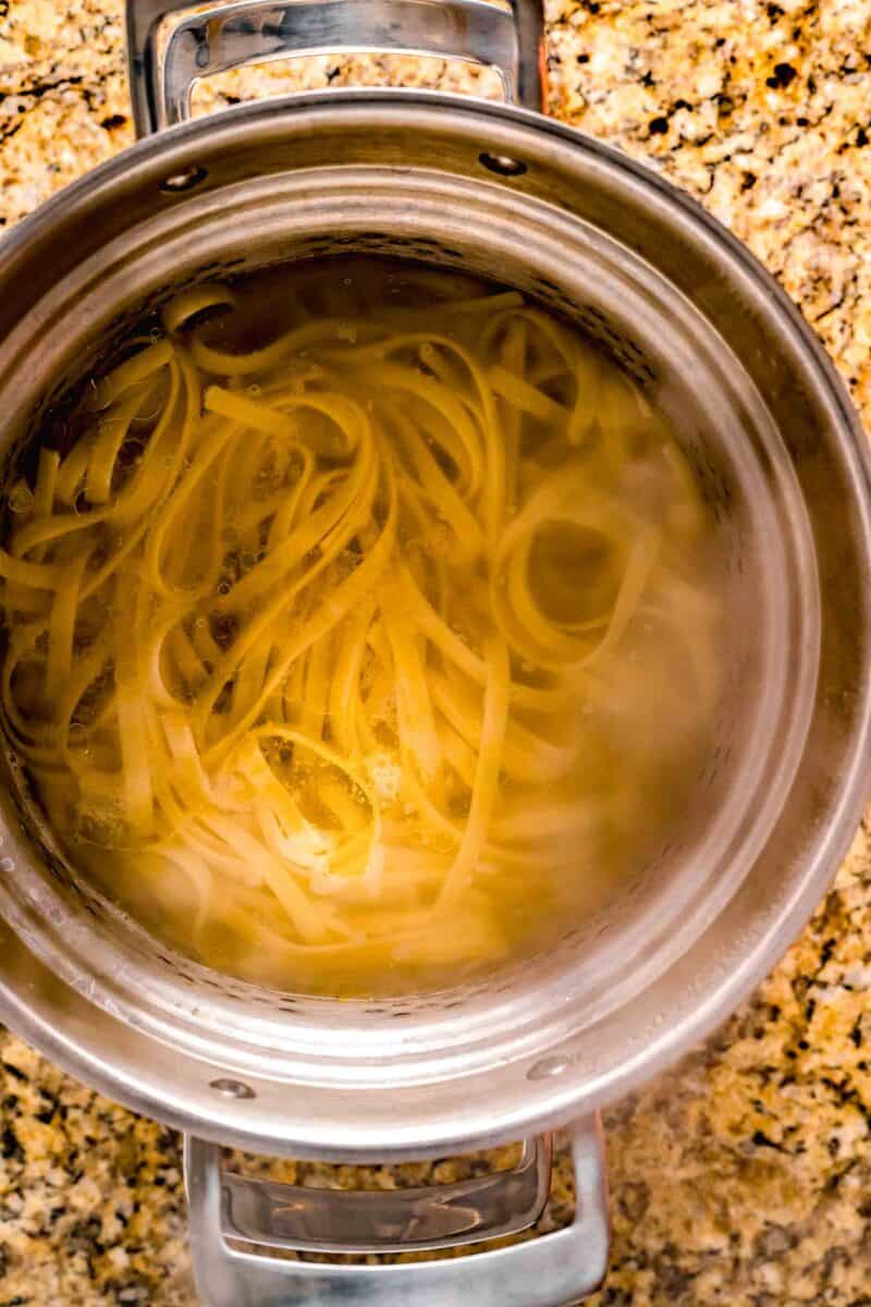 fettuccine noodles being cooked in a stainless steel pot with water