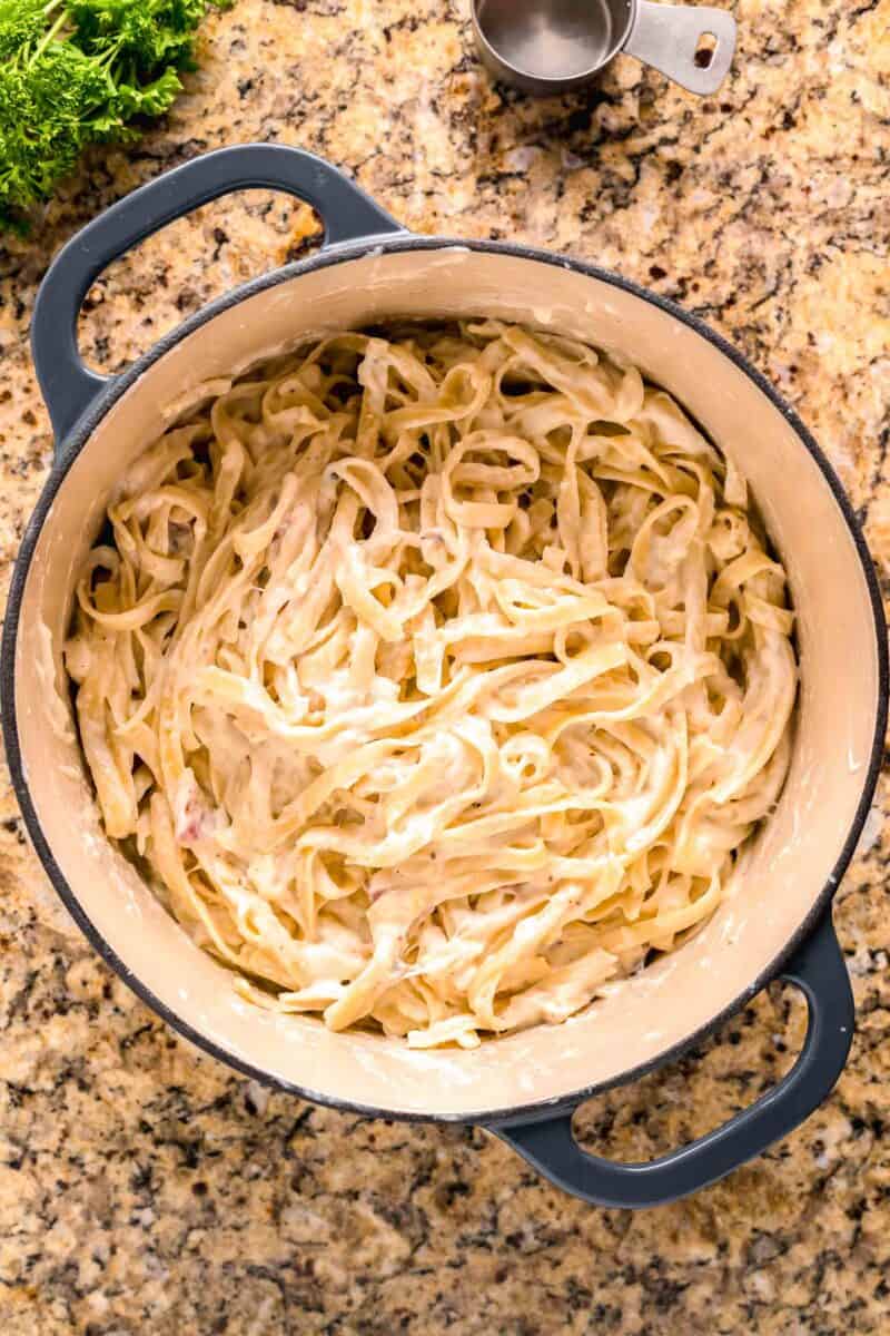 pasta tossed together in the cream sauce in a blue dutch oven