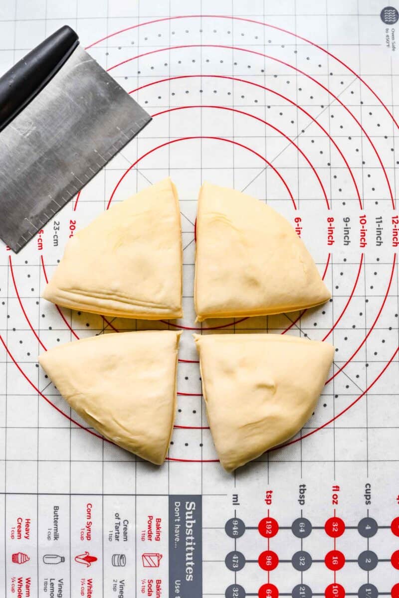 dough quartered on a silicone pastry mat with a metal pastry cutter next to it