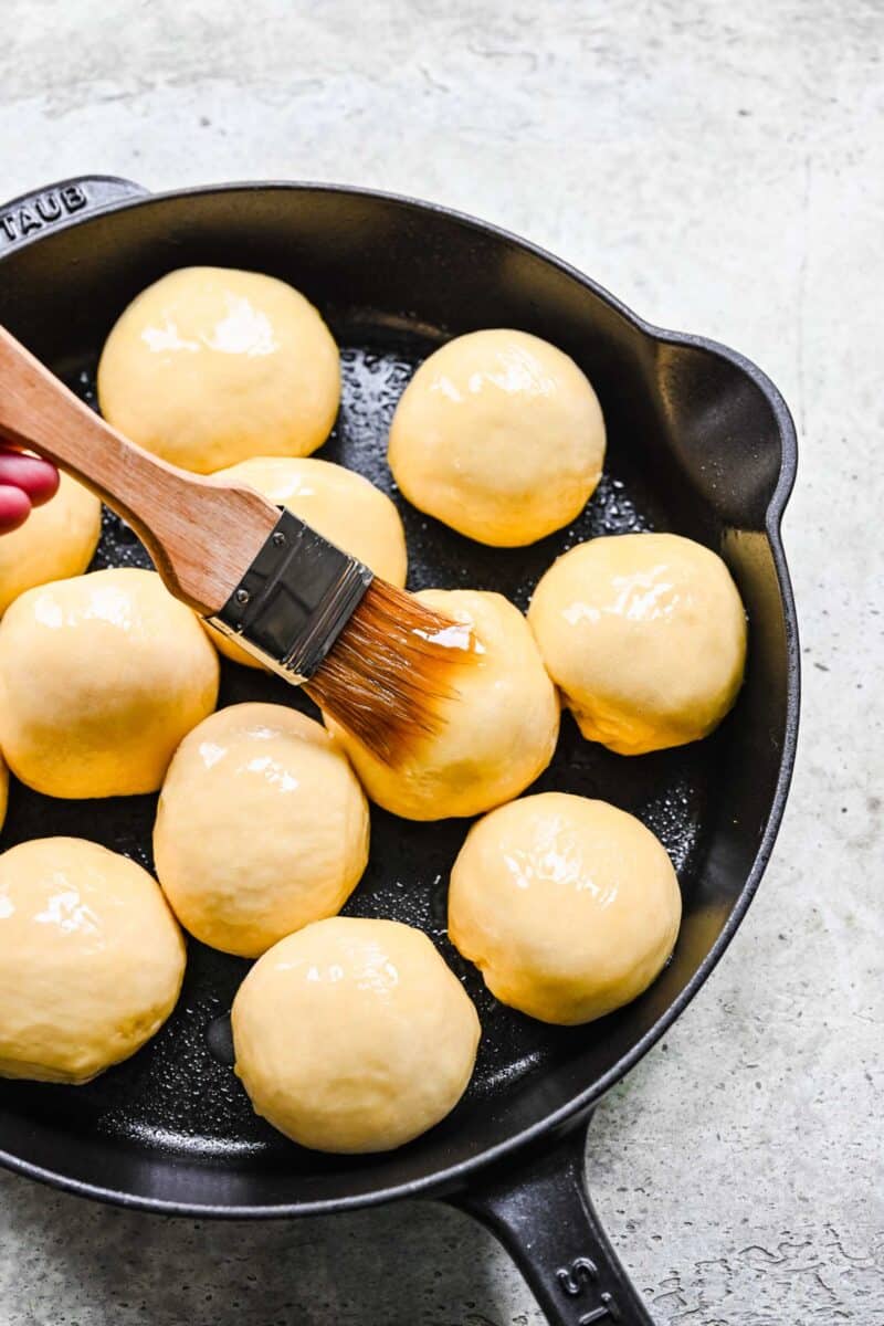 brushing honey butter with a pastry brush on the tops of the honey butter rolls in the cast iron skillet