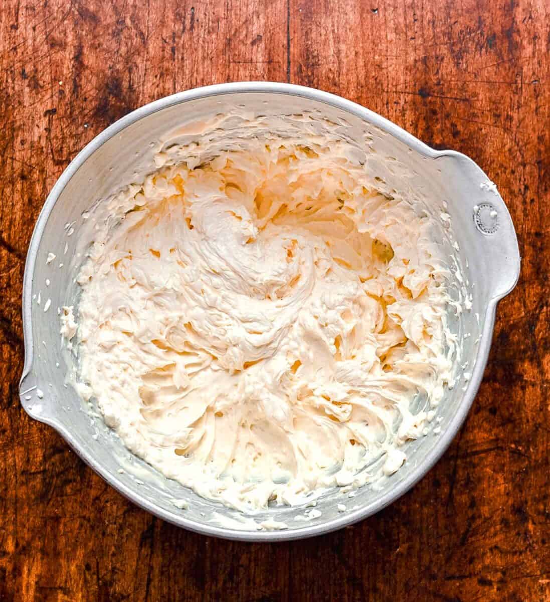 Creaming together cream cheese and mayonnaise in a mixing bowl.